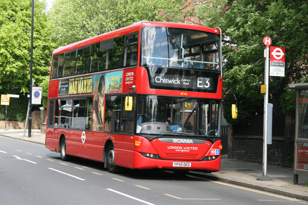 Red double-decker London bus on route E3 to Chiswick at a bus stop under leafy trees