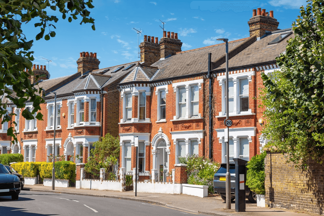 Row of red brick Victorian terraced houses with white bay windows and arched details on a Putney street